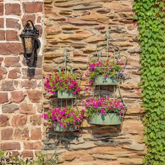 two hanging planters filled with pink flowers next to a brick wall