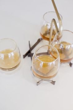 three glasses filled with liquid sitting on top of a white table next to metal spoons