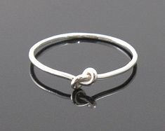 a silver ring with a knot on the middle and a heart in the middle, sitting on a black surface