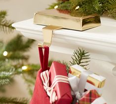 a christmas stocking hanging from a mantel with presents in it and evergreens on the mantle