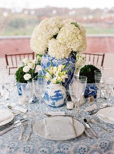 a blue and white vase filled with flowers on top of a dining table next to silverware