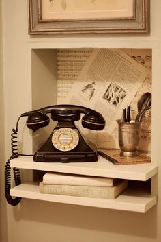 an old fashioned telephone is sitting on a shelf in the corner of a room with books and other items