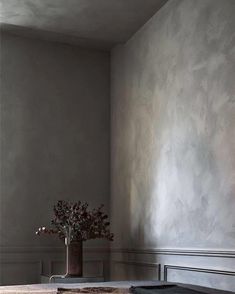 a vase with flowers in it sitting on a table next to a wall painted gray