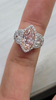 a woman's hand holding a fancy ring with two diamonds on it and an oval shaped pink diamond in the center