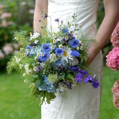 a bride holding a bouquet of blue and white flowers on her wedding day in the garden