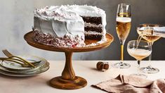 a cake with white frosting sitting on top of a table next to wine glasses