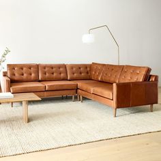 a brown leather couch sitting on top of a white rug next to a wooden table