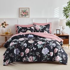 a bed with black and pink floral comforter set on it in a room next to a potted plant