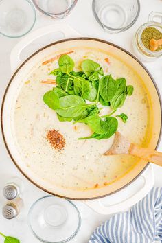 a bowl of soup with spinach leaves and seasoning in it on a table