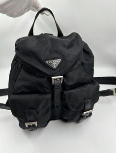 This vintage cult backpack from Prada is the ultimate throwback bag. When Prada released its original nylon backpack in 1984 it was an instant hit. This nylon backpack with a modern, minimalist design is decorated with the Prada enamel triangle logo. Underneath the flap with a leather strap and buckle, is a drawstring closure. There are two adjustable webbing shoulder straps with Prada branded buckles. There are two buckled pockets on the front. Inside features the iconic Prada logo lining and an interior zipped pocket for valuables. Lightweight, super cool yet durable and easy to wipe down! The backpack is in good overall condition with some minor signs of wear, mainly marks to the nylon and some creasing to the leather parts. Made in Italy. Height: 22cm Width: 25cm Depth: 12cm To ensure Modern Minimalist Design, Prada Nylon, Prada Logo, Logo Line, Triangle Logo, Vuitton Bag, Prada Bag, Chanel Bag, Modern Minimalist