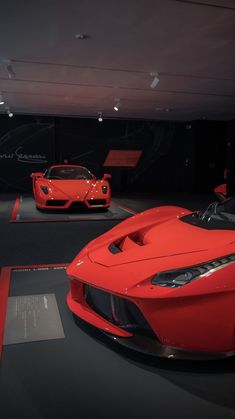 two red sports cars are on display in a showroom with black walls and flooring