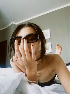 a woman laying in bed with her hands on her face while wearing sunglasses and looking at the camera