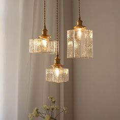 three lights hanging from a ceiling with flowers in the foreground and curtains in the background