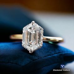 an emerald - cut diamond sits on top of a blue velvet cushion in front of a gold ring