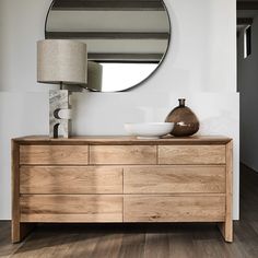 a wooden dresser with a round mirror above it and a lamp on the sideboard