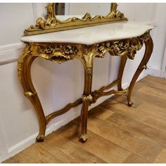 an ornate gold and white marble top console table with mirror on the wall behind it