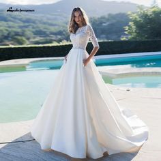 a woman standing in front of a pool wearing a wedding dress with long sleeves and an open back