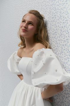 a woman in a white dress leaning against a wall