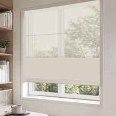 a window with blinds in the corner and bookshelves behind it, along with a coffee cup on a table