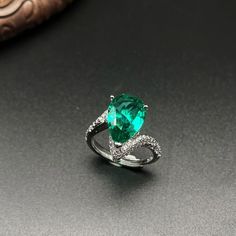 a ring with an emerald colored stone and diamonds on the side, sitting on a table