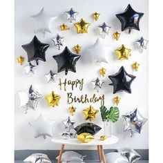 a birthday party with black, gold and silver balloons in the shape of stars on a white wall