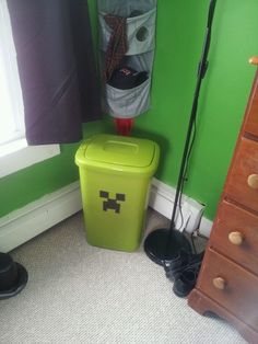 a green trash can sitting in the corner of a room next to a dresser and window