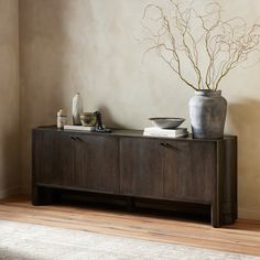 a vase with some branches on top of it next to a wooden cabinet in a room