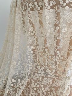 an embroidered sheer fabric with white flowers on the top and bottom, hanging in front of a window