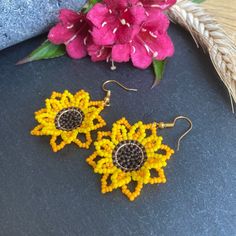 two yellow and black beaded sunflower earrings next to pink flowers