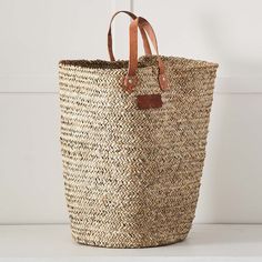 a large woven basket sitting on top of a white table next to a wall with a brown leather tag