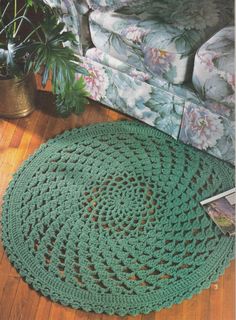 a green crocheted rug sitting on top of a wooden floor next to a couch