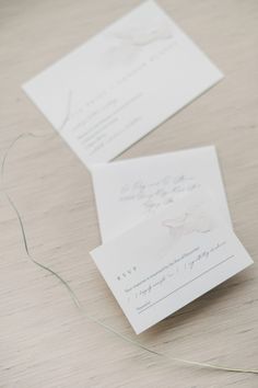 two white envelopes sitting next to each other on top of a wooden table with string