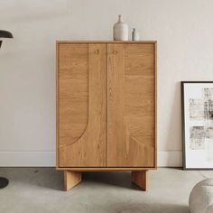 a wooden cabinet sitting on top of a floor next to a chair and table with vases