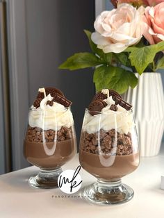 two glasses filled with dessert sitting on top of a table next to a vase full of flowers