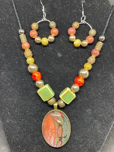 Unique Fluid art pendant and earrings, featuring greens and red in antique brass setting . This pendant is made from acrylic paint that dripped from my pour paintings. The paint dries and makes a skin which is positioned under a glass cabochon and then placed into the nickel free stainless steel bezel. The statement piece is in shades of red and green and the beads complement the colors, all in an antique brass setting. Earrings match. Color is my passion and each is unique in its own way. Beads are glass and plastic and the cord is wax coated. The length is adjustable with a sliding knot. Handmade Artsy Bronze Jewelry, Artsy Handmade Bronze Jewelry, Multicolor Copper Jewelry Gift, Multicolor Copper Jewelry For Gift, Multicolor Copper Jewelry For Gifts, Multicolor Hand Painted Metal Jewelry, Hand Painted Multicolor Metal Jewelry, Artistic Copper Jewelry, Artistic Multicolor Copper Jewelry