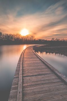 the sun is setting over a body of water with a wooden dock in front of it