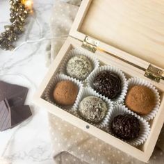 four chocolate truffles in a wooden box on a table with christmas lights and decorations