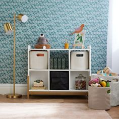 a white shelf with baskets and toys on it in front of a blue wallpaper