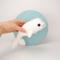 a hand holding a small white stuffed whale on top of a blue buttoned object