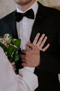 a man in a tuxedo holding a bouquet of flowers and wearing a ring