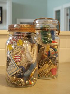 two glass jars filled with different types of toys and magnets on top of a counter