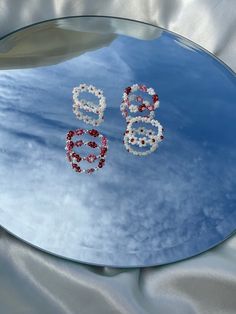 the reflection of two red and white earrings on a mirror with clouds in the background