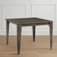 a small square table with metal legs on a wooden floor in front of a white wall