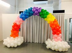 a rainbow arch made out of balloons in front of a drape curtain with curtains behind it