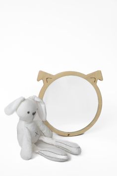 a white stuffed animal sitting next to a wooden frame with a mirror behind it on a white surface