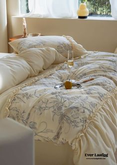 a bed with white comforter and pillows in front of a window, next to a glass of wine