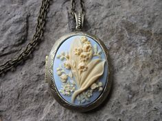 "Beautiful cameo locket, choose bronze, antiqued silver, or silver (other colors and styles are available in my shop so please do browse The cameo is a gorgeous lily of the valley. Stunning colors. cream on sky blue. The bronze and silver plated lockets are Victorian style with beautiful scroll on both the front and back about 2\" long, please see the photos. They can hold two photos, a treasured keepsake or both. Pass down from generation to generation The bronze locket includes a 24\" adjustab Antique Brass Locket Necklace For Wedding, Nickel-free Brass Locket Necklace For Wedding, Bronze Brass Locket Necklace For Wedding, Antique Finish Brass Locket Necklace For Wedding, Bronze Locket Necklace With Vintage Charm For Wedding, Bronze Vintage Charm Jewelry For Wedding, Elegant Bronze Locket Necklace For Wedding, Bronze Antique Finish Jewelry For Wedding, Bronze Antique Finish Wedding Jewelry