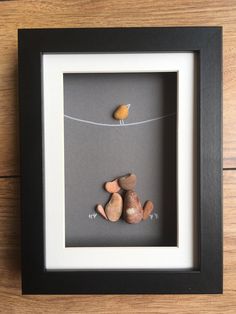 two rocks and a bird on a wire in a shadow box with a black frame