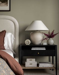 a nightstand with a lamp on top of it next to a bed