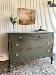 an antique dresser painted green in a room with striped wallpaper and painting on the wall